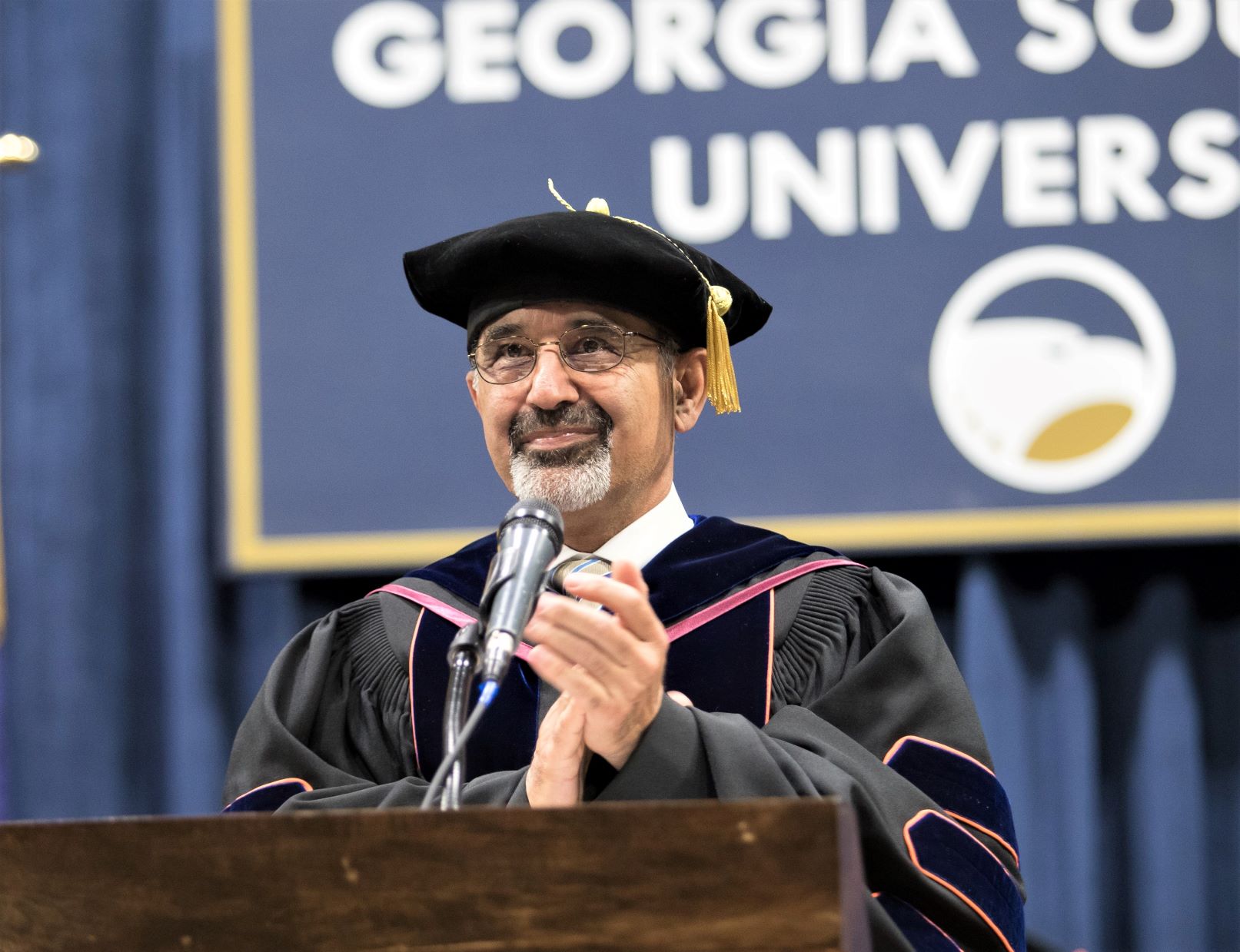 adult male wearing graduation regalia clapping his hands